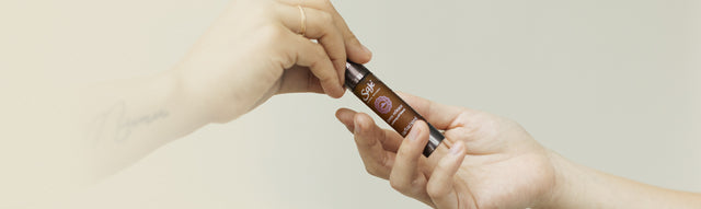 A person hands a Saje remedy roll-on to another person as a gift.