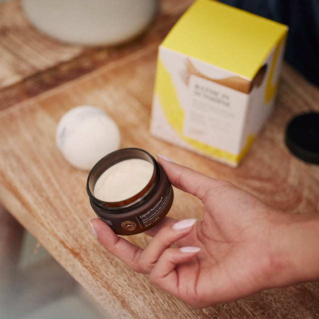 Person holding liquid sunshine body butter with lid off