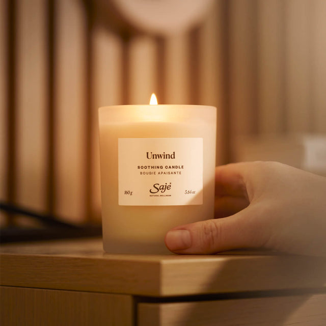 A lit unwind candle sitting on a wooden side table.