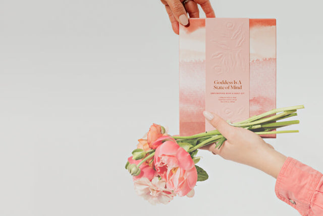 A young woman's hand passing a limited edition gift box and flowers to her mother's hand.