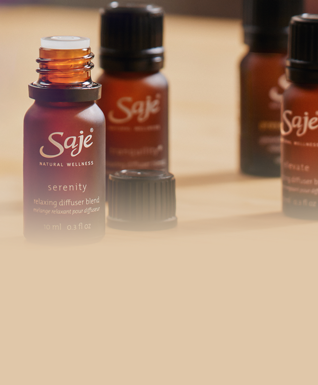 4 Saje diffuser blends are styled on a wood table. A white Aroma Om Diffuser is in the background.