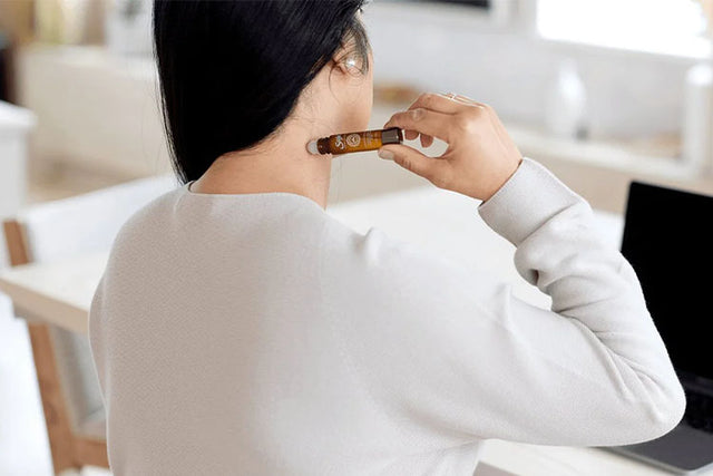 Person at their desk applying a roll-on to their neck.