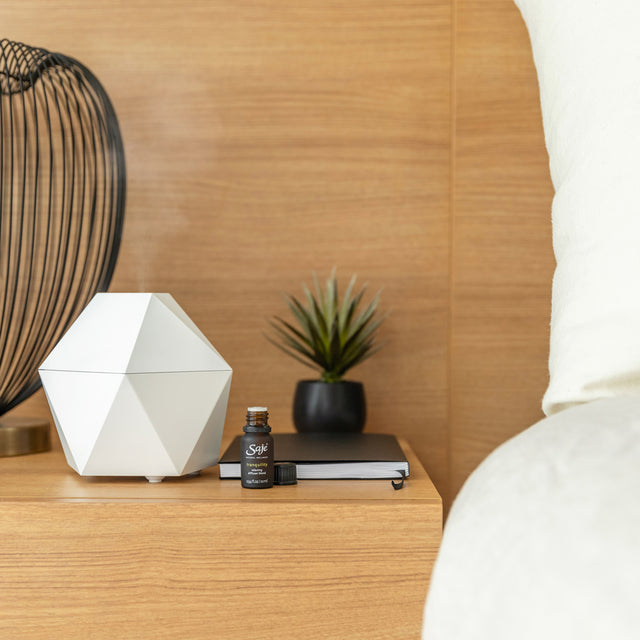 White Aroma Be Free diffuser on wood table with tranquility diffuser blend bottle.