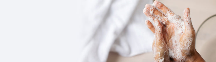 Close up of hands being washed with foaming hand soap with a fresh, white towel in the back