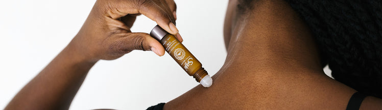 Woman applying Saje Peppermint Halo Roll-on to her upper trap muscles
