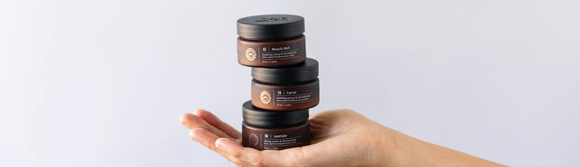 A person holding a stack of saje body butters