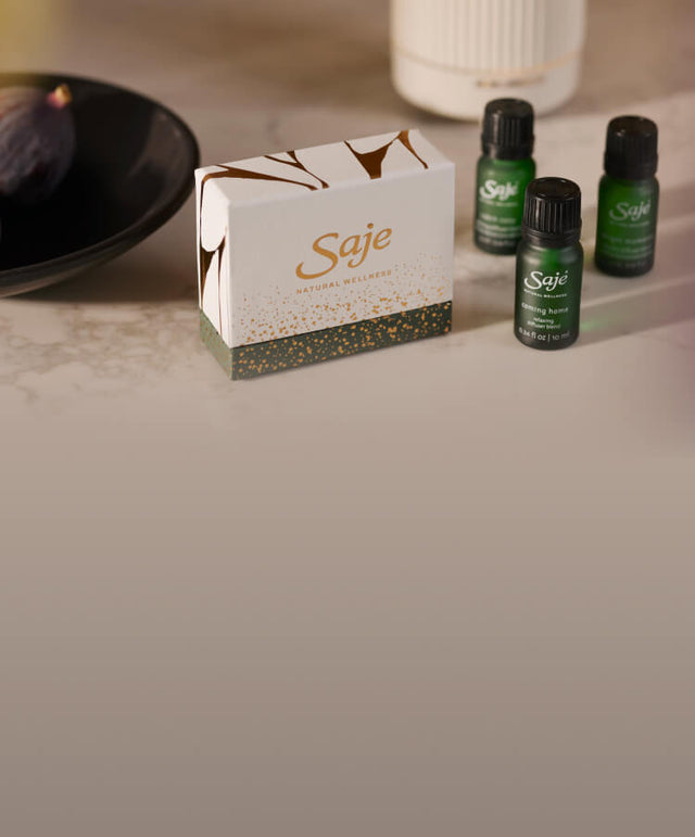Three seasonal diffuser blends, a holiday blend box, and a decorative bowl of figs are styled on a marble countertop.