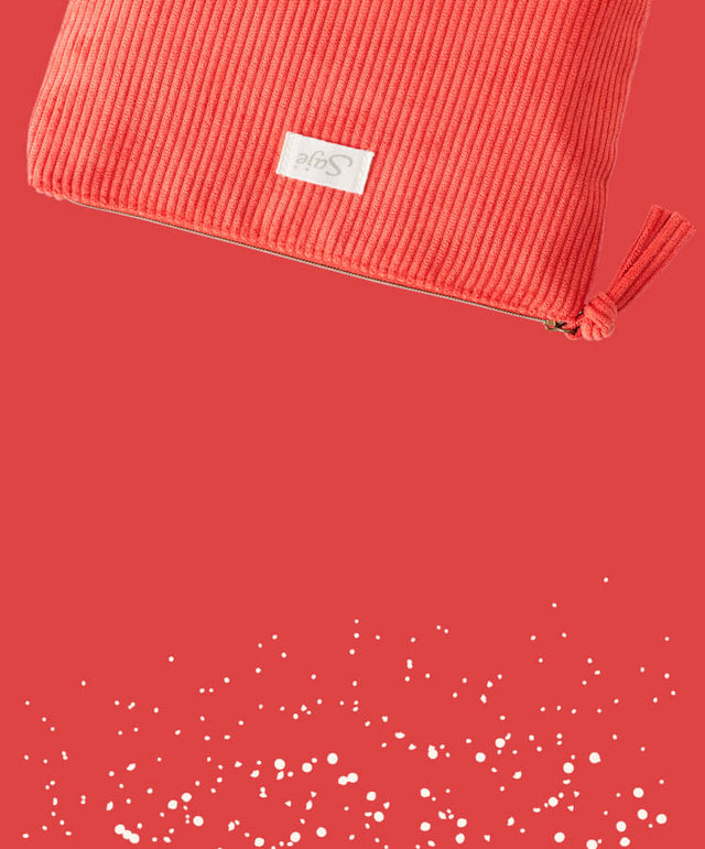 A red corduroy cosmetic bag with tassel zipper detailing against a red background with off-white flecks.