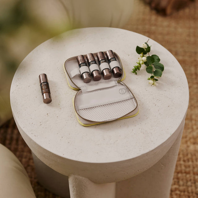 A Saje Pocket Farmacy unzipped with five roll-ons inside sitting on a cement side table