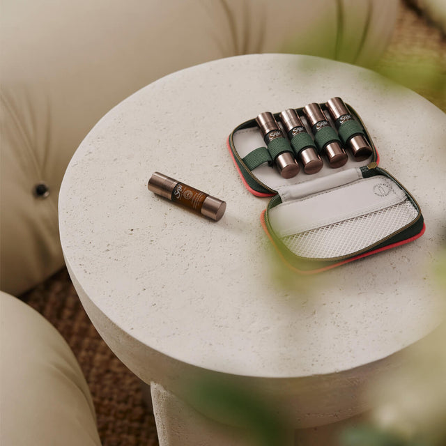 A Saje Pocket Farmacy unzipped with five roll-ons inside sitting on a cement side table