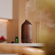 Aroma Rise Amber Glass diffuser sitting on the counter next to a Saje diffuser blend with cap off
