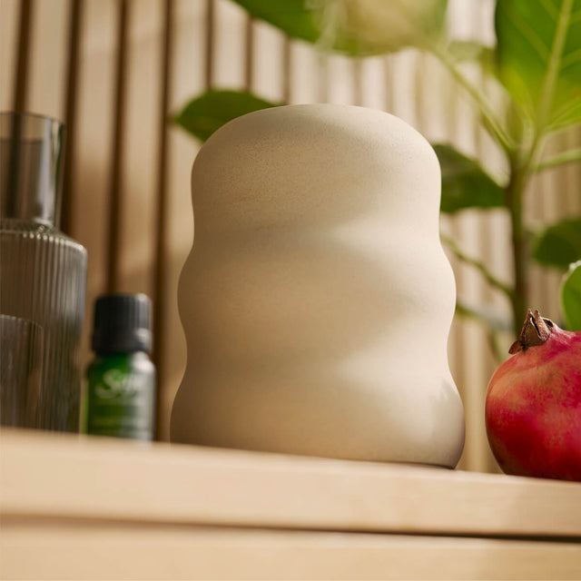 Aroma Wave diffuser sitting on a wooden counter next to a Saje diffuser blend and a pomegranate