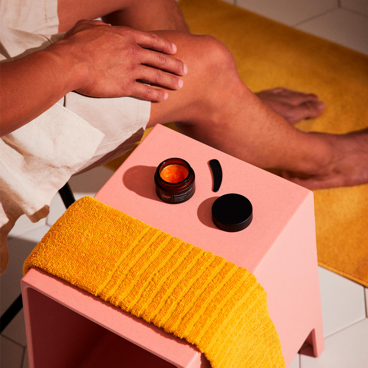 Person sitting next to open Extra Strength Balm Warming Pain Relief ointment on a salmon side table