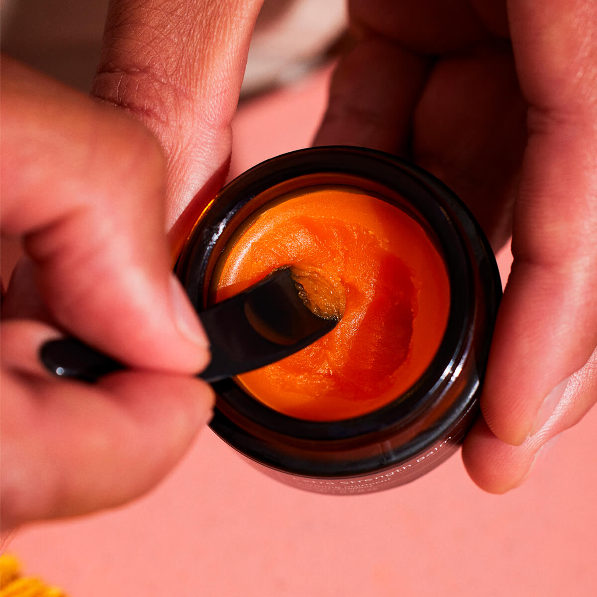 Hands with applicator and Extra Strength warming balm, on a salmon background