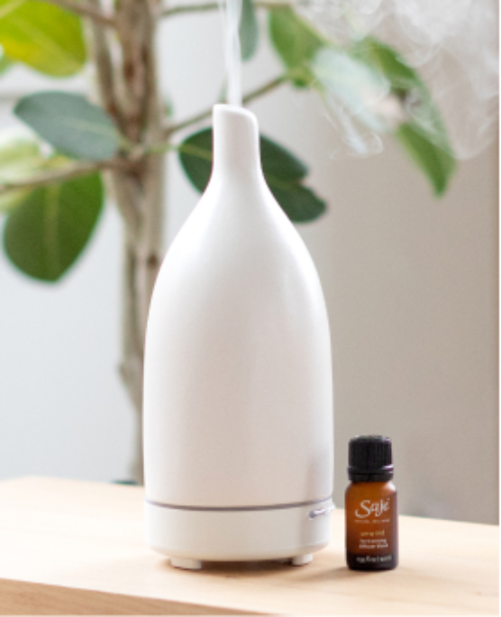 White Aroma Om is styled with a diffuser blend on a wood table. 