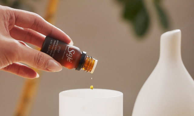 A woman adds droplets of Yoga diffuser blend to a white Aroma Om diffuser. 