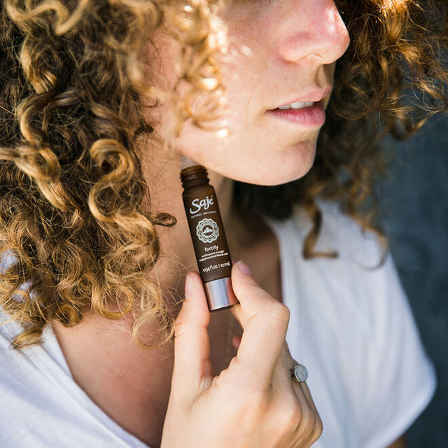 A woman with very curly hair applying Fortify roll-on to the side of her jawline