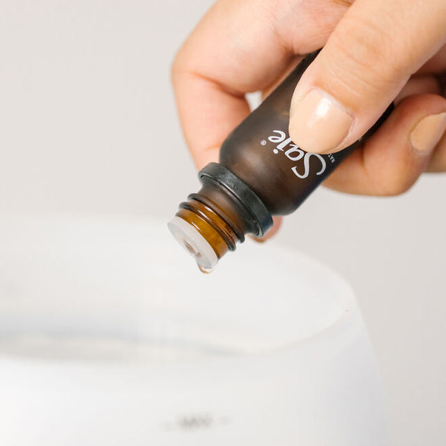 a hand dropping essential oil from a diffuser bottle into a diffuser water tank