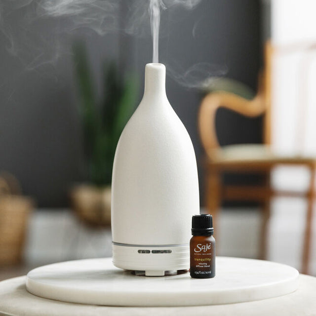 Tranquility 0.34 fl oz relaxing diffuser blend bottle with the cap on next to an Aroma Om White diffuser