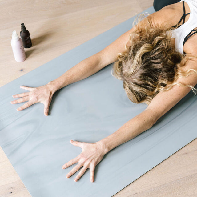 Yoga Mat Mist 6.08 oz purple bottle beside a person practicing yoga