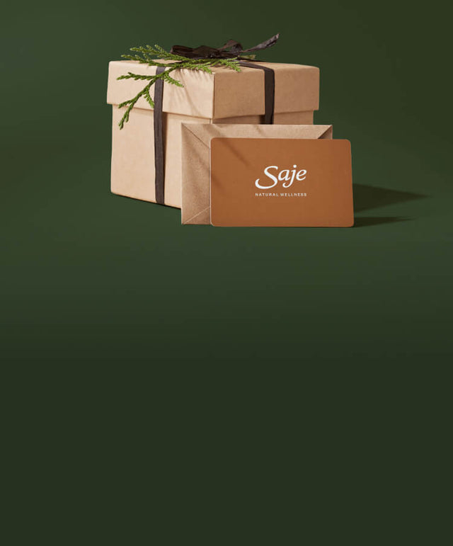 A Saje gift card is propped up on a decorative cardboard giftbox against a plain green background.