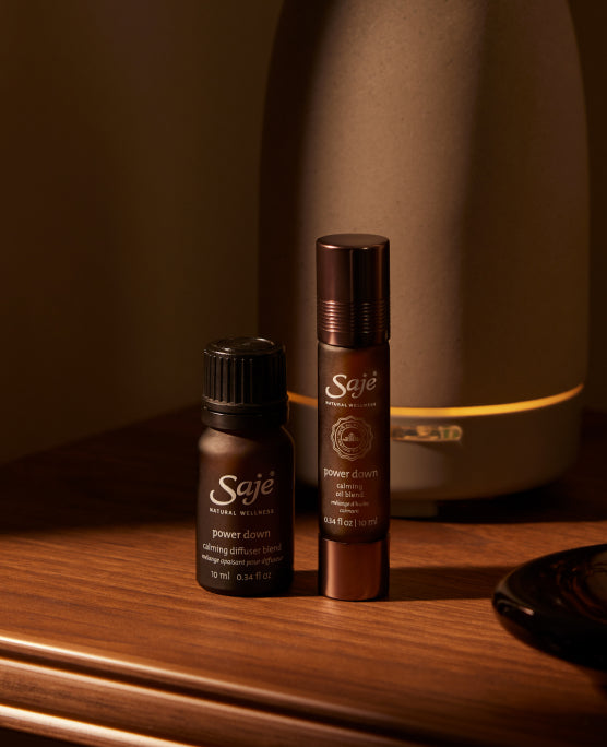 Power Down Diffuser Blend and Roll-On on a brown wooden counter in a dimly lit room with a diffuser behind.