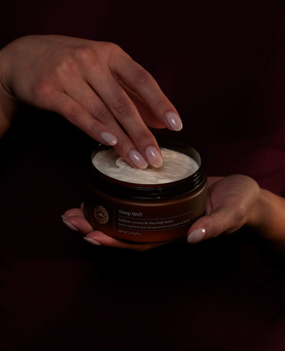 A person’s hand and two fingers scooping some creamy white moisturizer out of a round container.