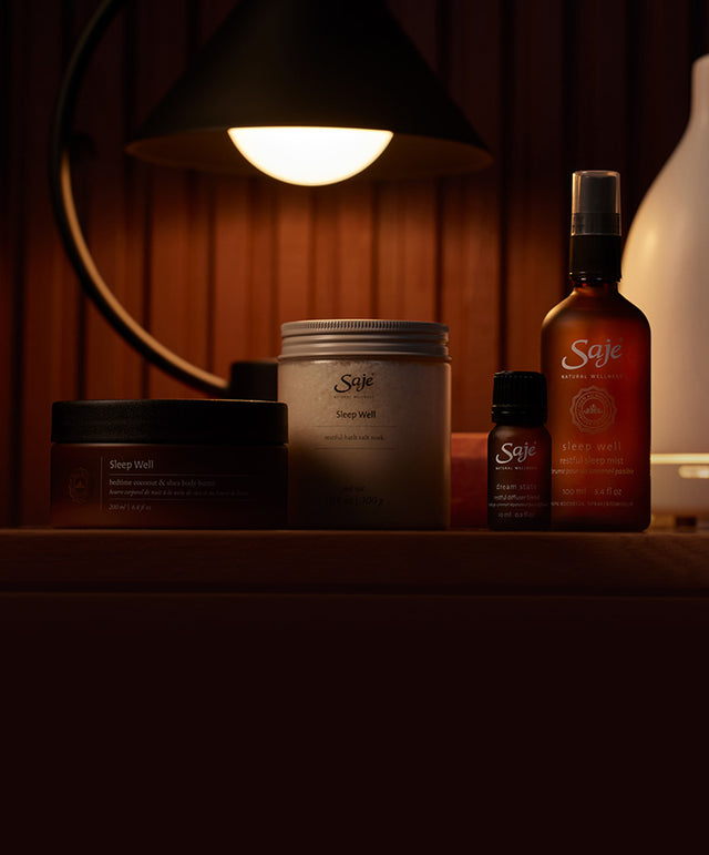 A collection of Saje sleep products and a diffuser against a dimly lit wooden backdrop.