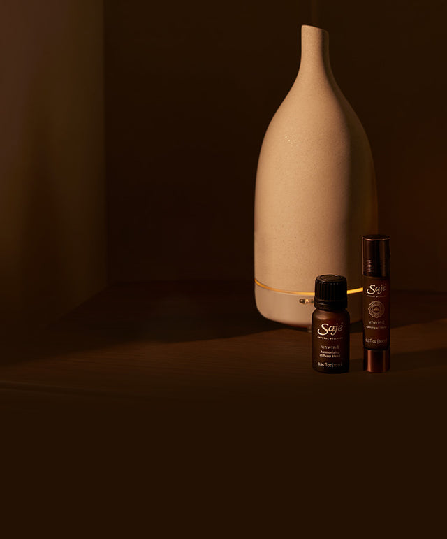 A collection of Saje sleep products and a diffuser against a dimly lit wooden backdrop.