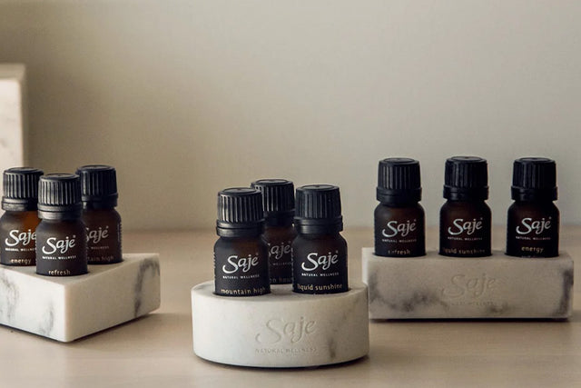 A stack of essential oil holders in the shape of a circle, triangle and rectangle sits beside three Saje essential oils.