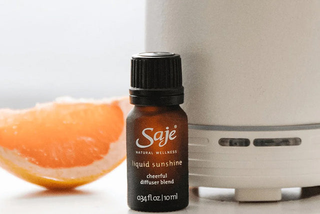 Liquid sunshine diffuser blend, White Aroma Om diffuser and orange slice on a white background.