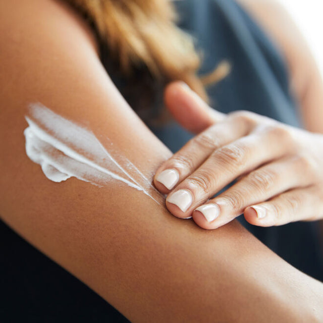 A manicured hand applying lotion to the bicep area
