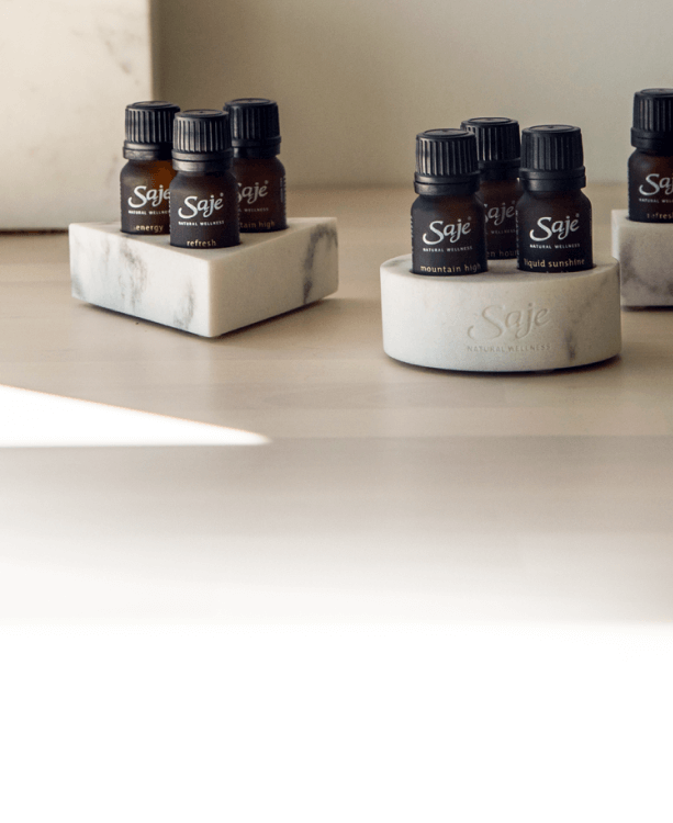 A stack of essential oil holders in the shape of a circle, triangle and rectangle sits beside three Saje essential oils.