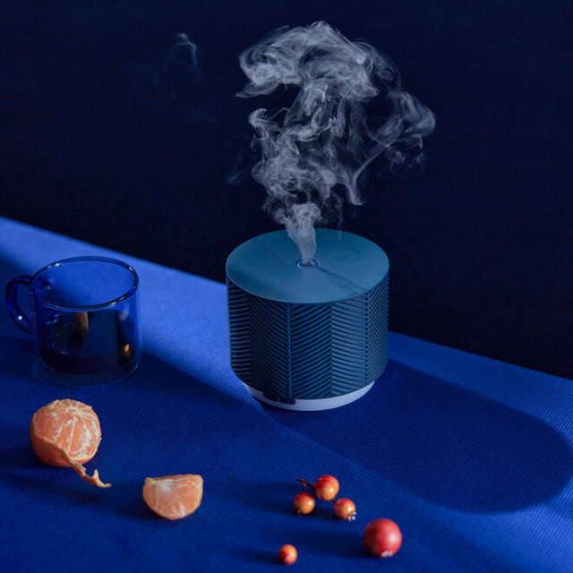 Denim Blue Aroma Nook diffuser diffusing mist on dark blue background.