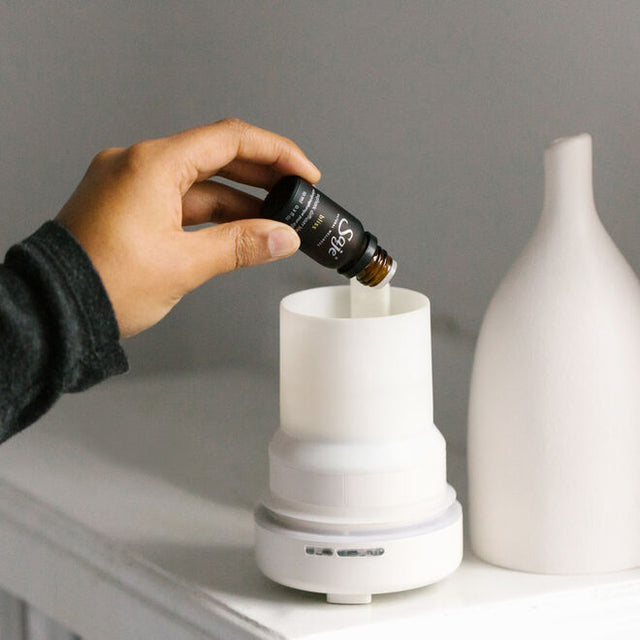 Person dripping diffuser blend oil into a White Aroma Om diffuser 