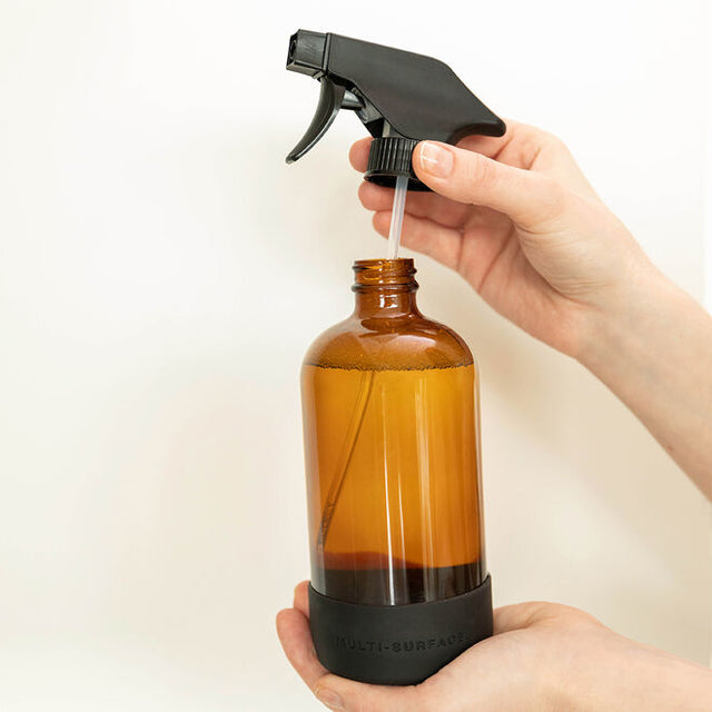A pair of hands showing that the reusable glass spray bottle nozzle can be removed to refill the bottle