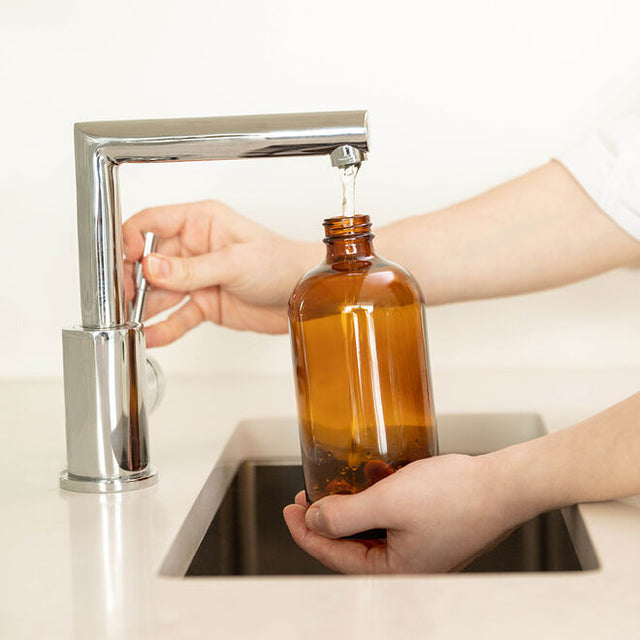 Person filling the cleaning reusable glass bottle with water at a sink