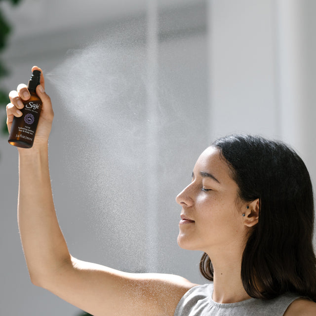 A woman with her eyes closed misting over her head with Rose mist