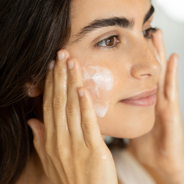 A woman gently massaging the cleanser in a circular motion over their face 