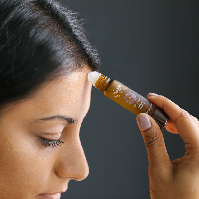 a woman applying the cleanse roll-on to the front of her forehead by her hairline