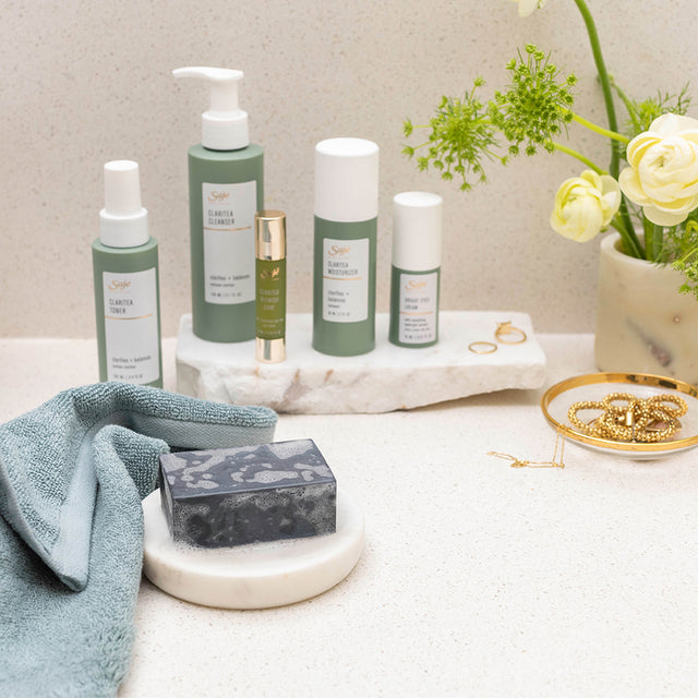 Claritea skincare line by Saje on bathroom counter with plant, jewelry and towel
