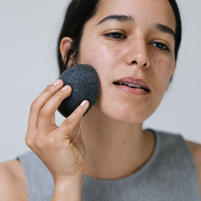 A person gently exfoliating their face with Konjac Kare bamboo charcoal purifying vegetable fibre sponge 