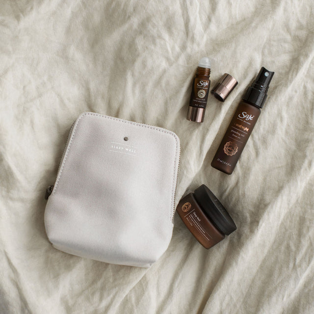 Sleep Well kit with grey bag, roll-on, body butter container and goodnight mist bottle flatlay on grey bedding