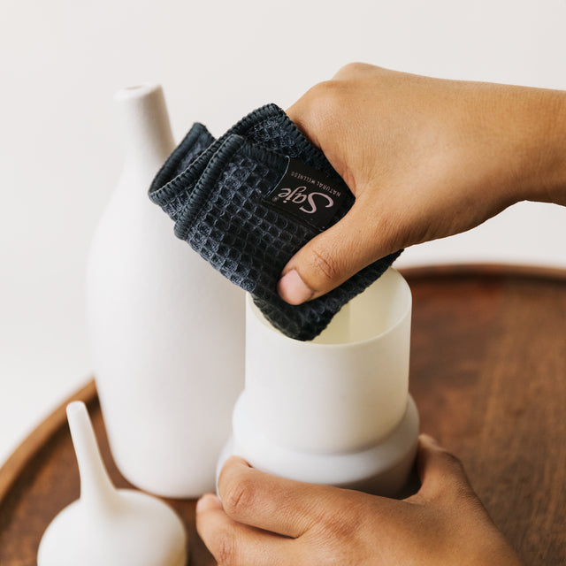 A pair of hands using the grey cloth to wipe the inside of a diffuser water tank